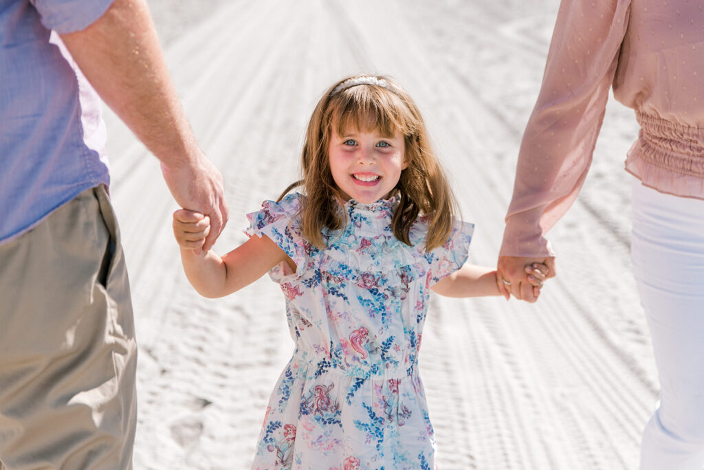 A young girls holds her parents hands as they walk during Coronado Beach family photos