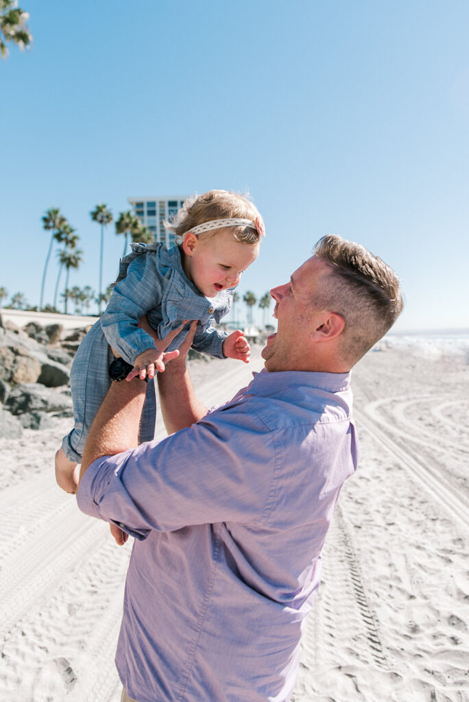 Dad picks up toddler with a large smile on his face at Coronado Beach in San Diego, California