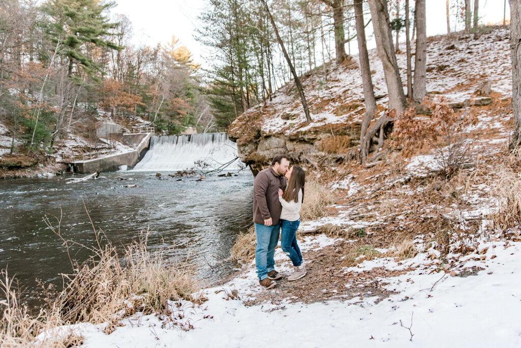 A couple kisses near a waterfall during their winter engagement photo session