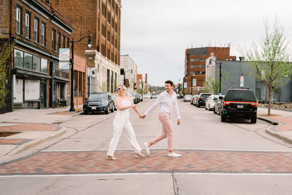 A couple crosses Barstow Street during a downtown Eau Claire Engagement Session
