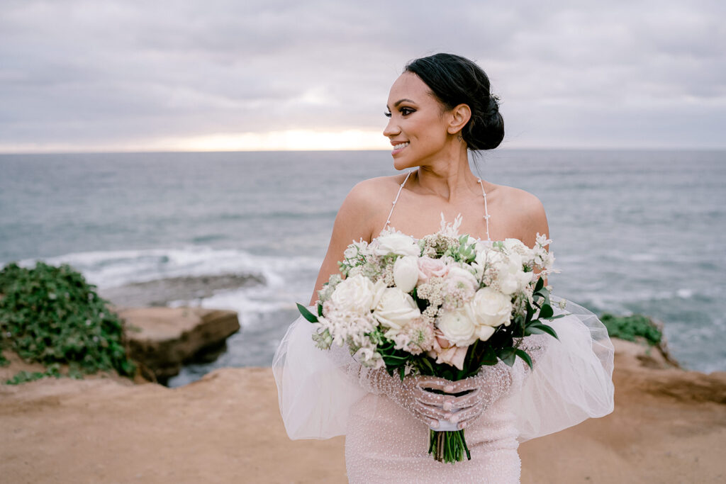 Bride in beaded gloves holds her wedding bouquet at Sunset Cliffs in San Diego