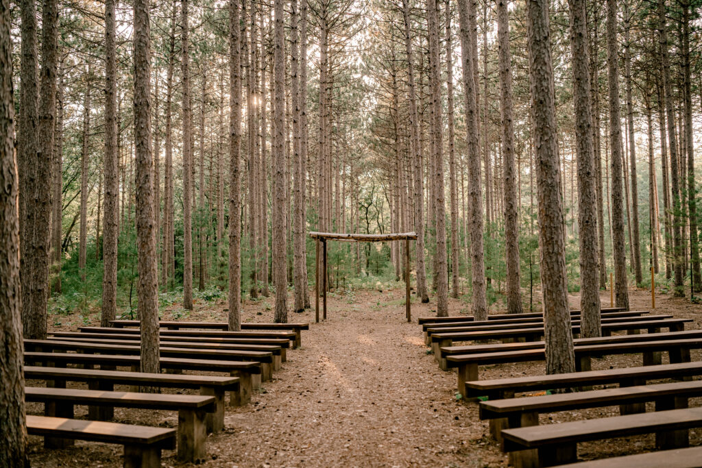 Benches line an aisle of a wedding ceremony location in a pinewood forest at Burlap and Bells wedding venue in Black River Falls, WI. 