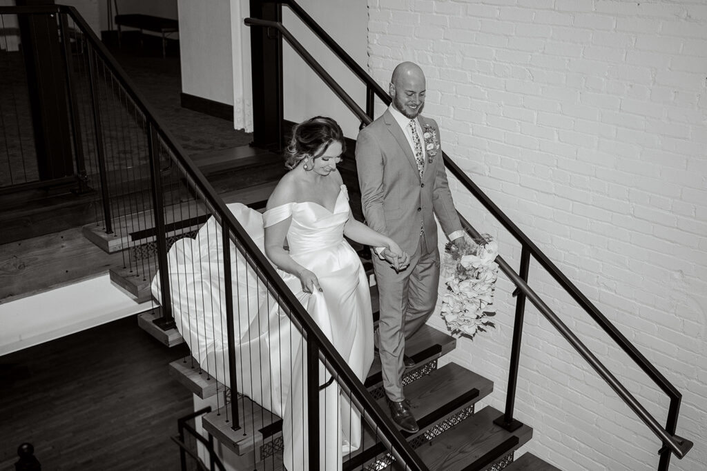 A Bride and Groom walk down the stairs at The Confluence Hotel while holding hands