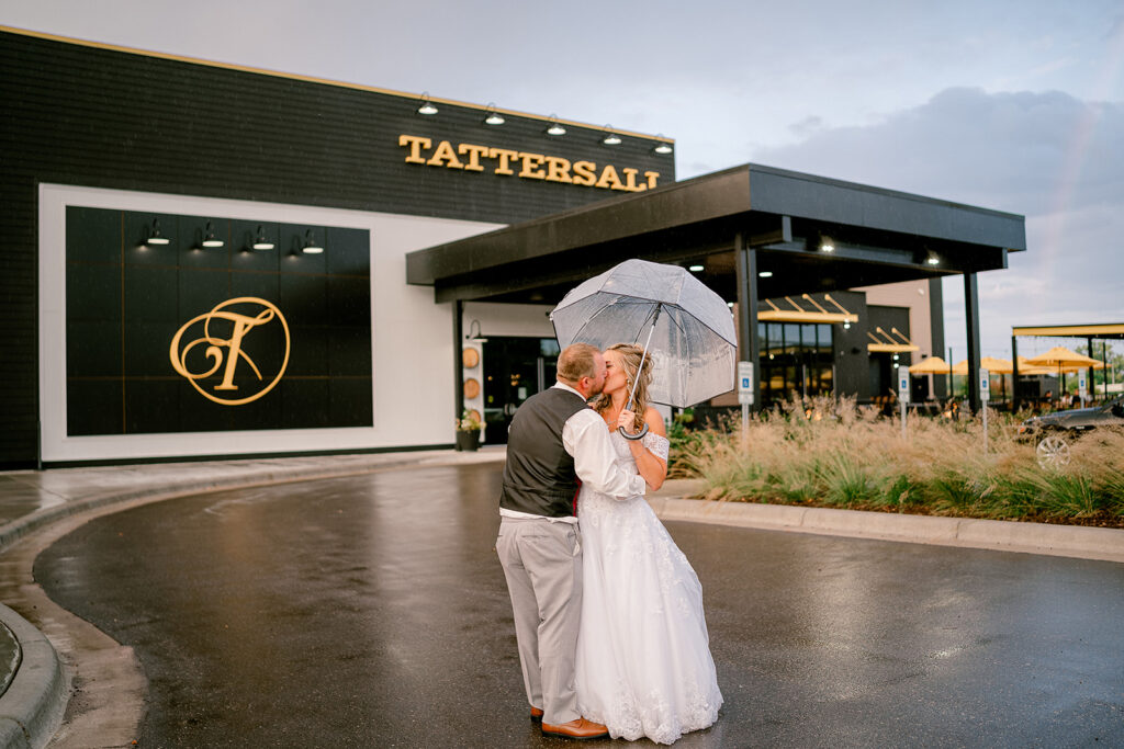 A couple kisses under a clear umbrella in front of Tattersall Distilling in River Falls, Wi. 